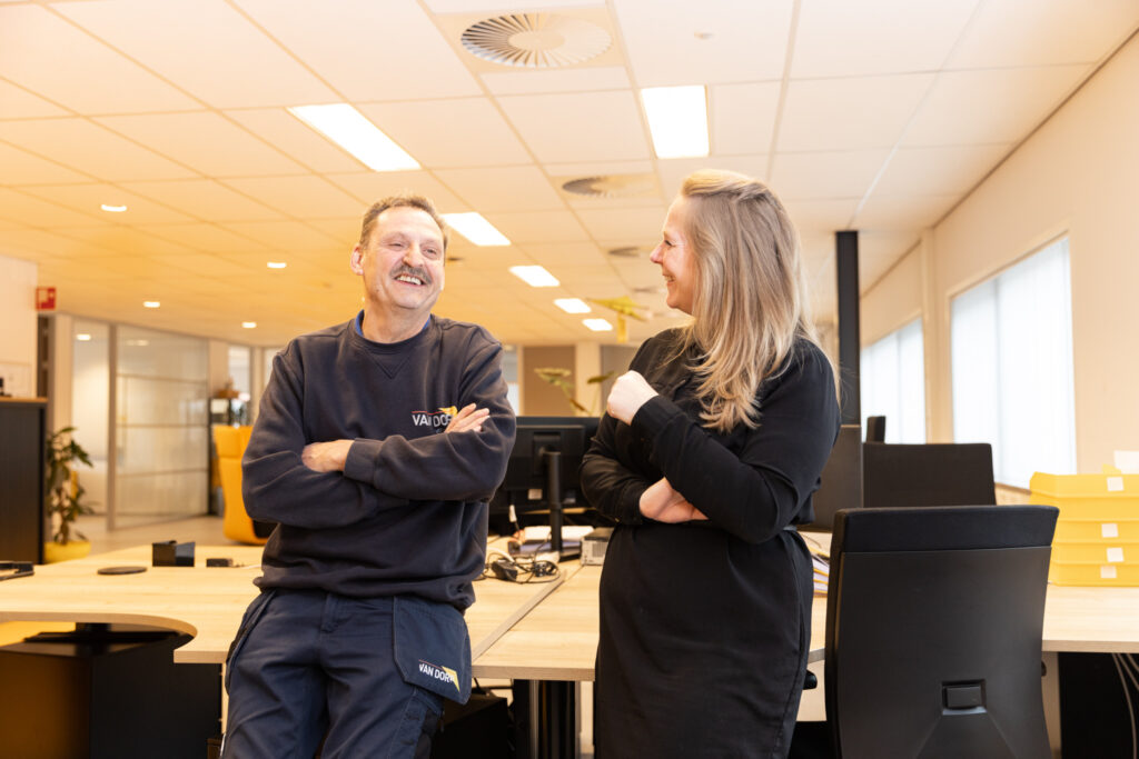 Technisch beheerder en contractmanager van Van Dorp lachen en praten met elkaar in een kantooromgeving.