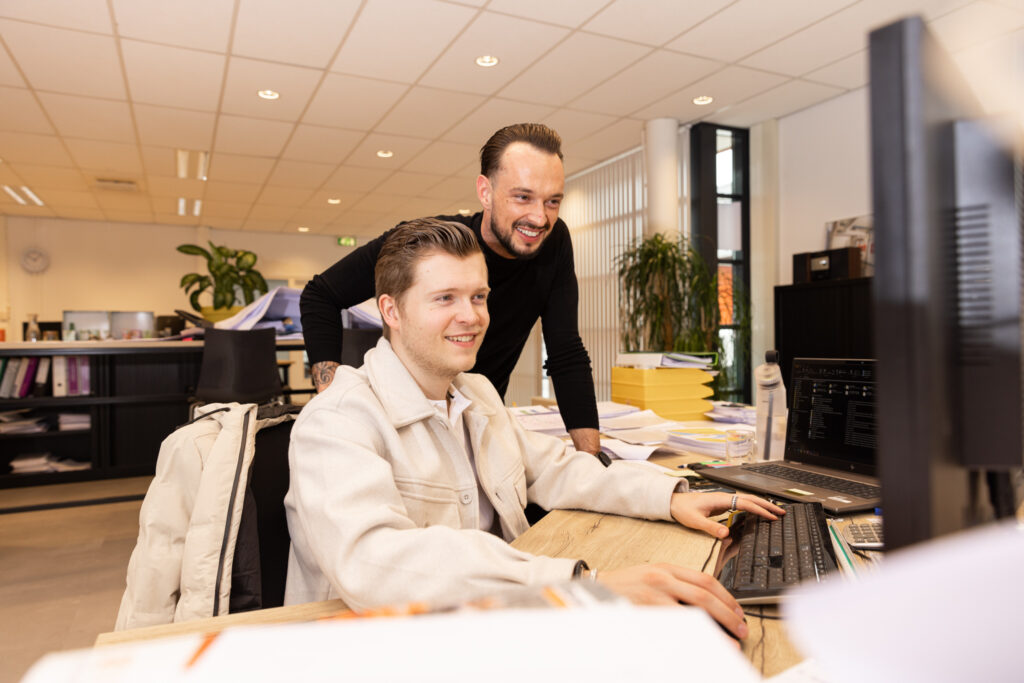 Twee collega’s achter een bureau kijken samen naar een computerscherm in een kantooromgeving