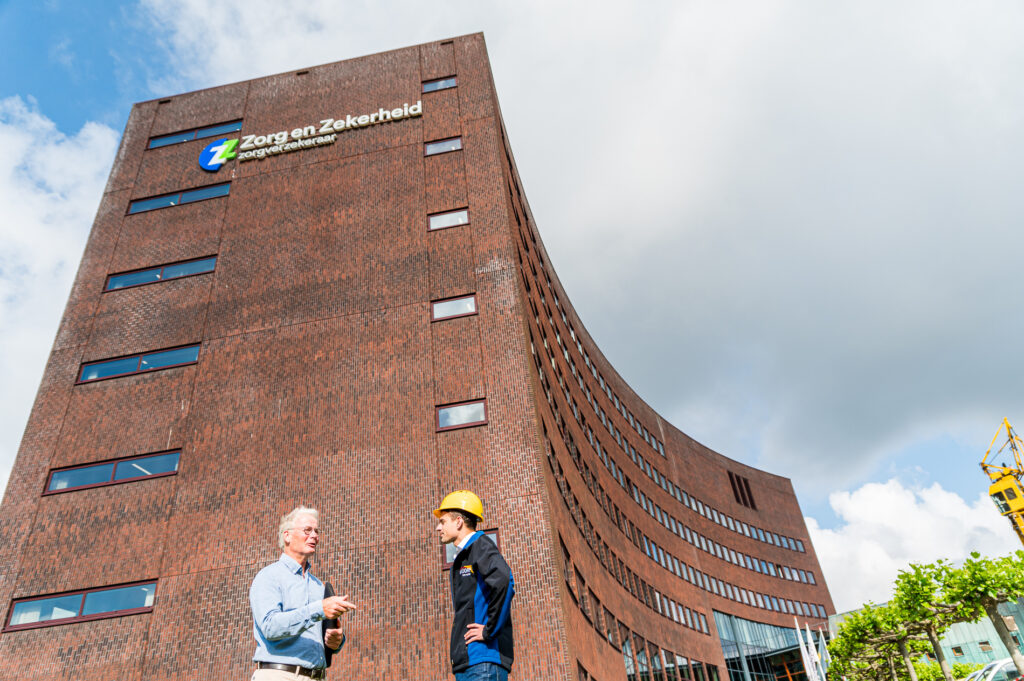 Medewerker van Van Dorp met veiligheidshelm in gesprek bij het hoofdkantoor van Zorg en Zekerheid.