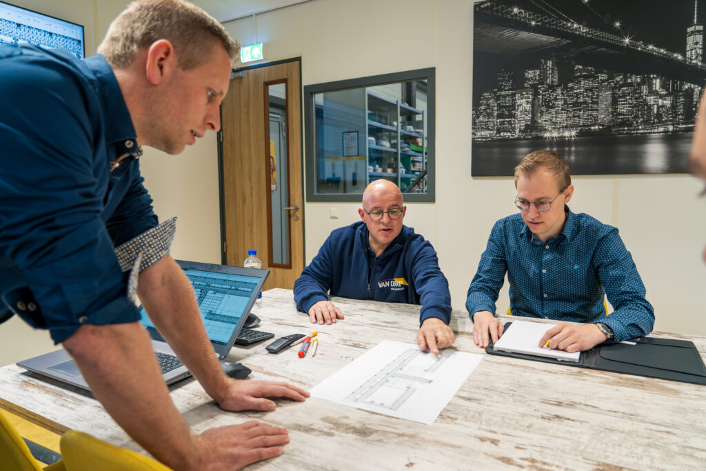 Drie collega’s van Van Dorp bespreken technische tekeningen aan een vergadertafel.