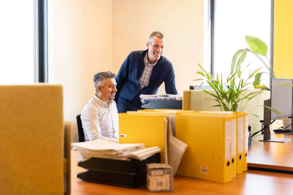 Twee collega’s praten en lachen samen achter een bureau