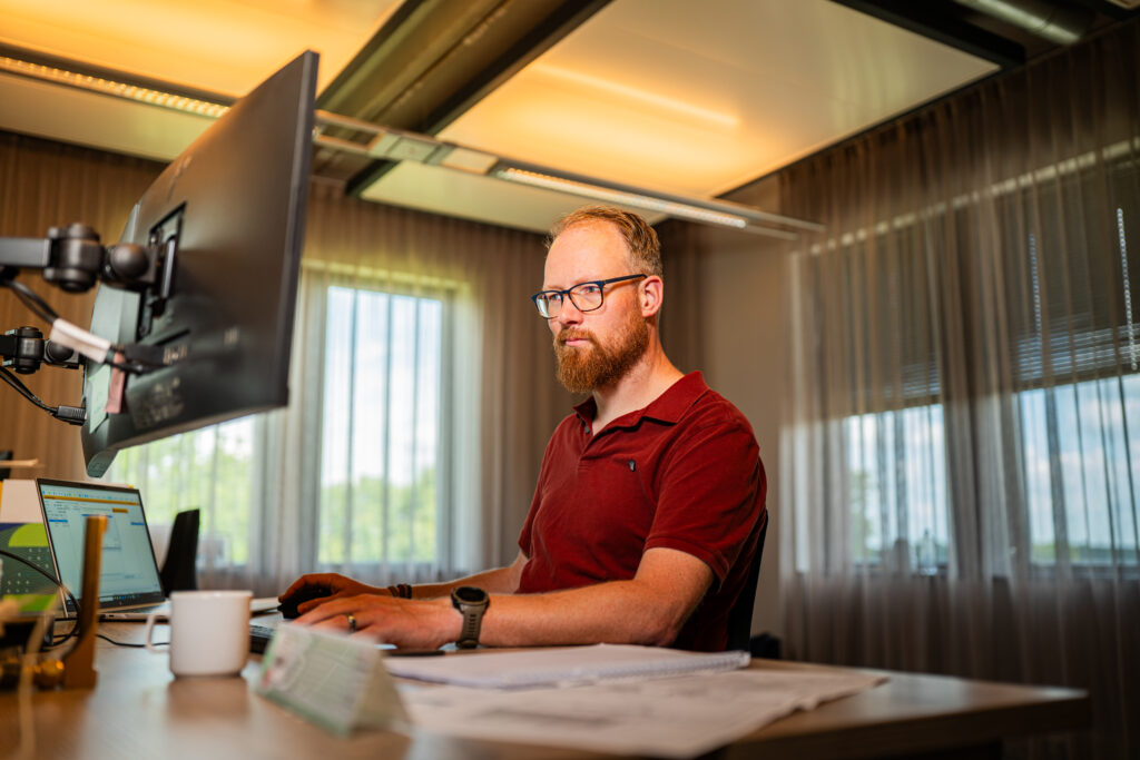 Projectleider achter een bureau werkt geconcentreerd op twee computerschermen in een kantooromgeving